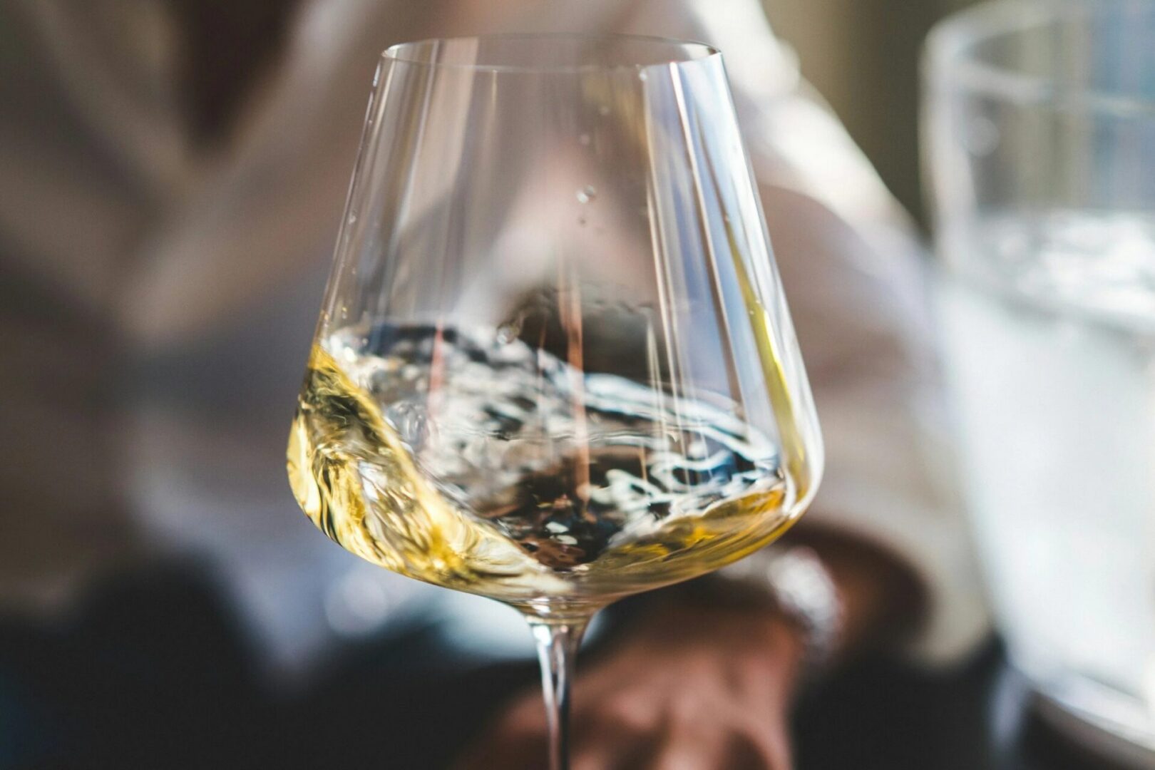 Person holding a glass of white wine in their hand, with another glass of the same wine to the right