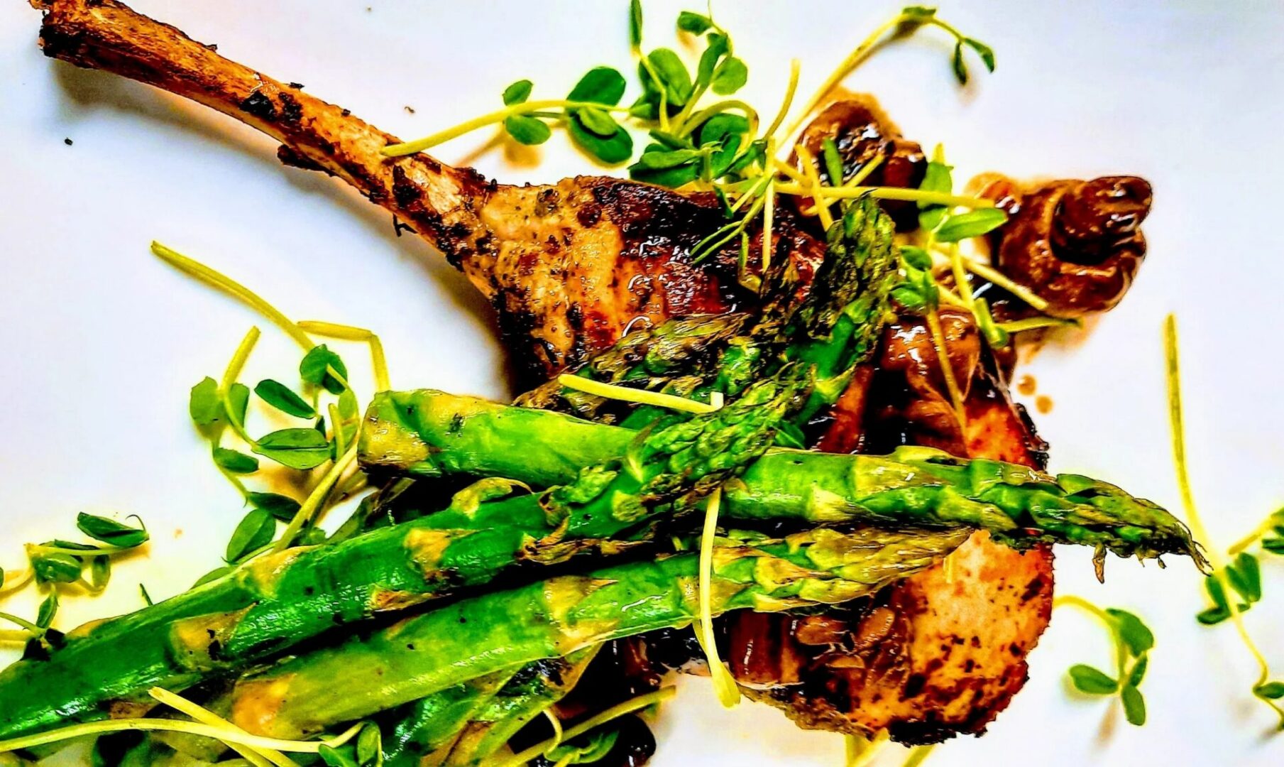 White plate topped with grilled lamb chops and asparagus, garnished with a lemon-thyme sauce